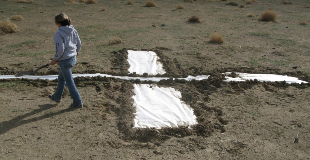 photograph of a good ground survey target Figure 2a: This target is effective because it was created on even terrain, away from buildings and trees, and it contrasts the ground colour.
Improvements: The accuracy could be improved if the photo included the GPS equipment on the target. The dirt that is weighing down the tarp could blow over and cover the tarp in strong winds. Rocks are recommended when possible.